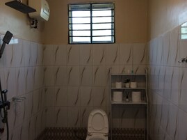 A bathroom with a toilet, a shelf with toiletries, a window, and a towel rack.