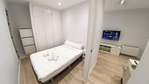 Une chambre à coucher moderne, équipée d’un lit, d’une armoire, d’une télévision et d’un bureau.