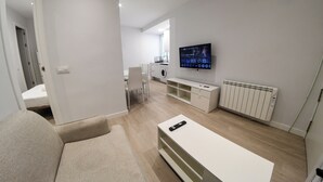 Un salon moderne avec un canapé, un téléviseur fixé au mur, un lave-linge et un radiateur.