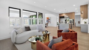 A modern living room with a sofa, armchairs, and a coffee table. There is a kitchen area with a dining table and chairs.