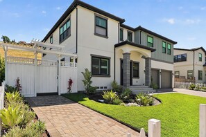 A modern two-story house with a well-maintained lawn, a brick pathway, and a white fence.