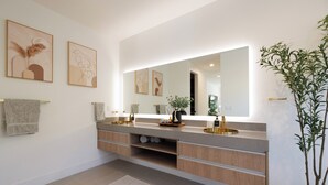 A modern bathroom with a large mirror, two sinks, wooden cabinetry, and a potted plant.