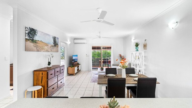 A modern kitchen with white cabinets, a wooden dining table, and a ceiling fan. - Bright Cozy Apartment Central - Modern (Darwin)