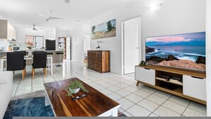 A modern living room with a large TV, dining area, and kitchen. - Bright Cozy Apartment Central - Modern (Darwin)