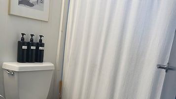 A bathroom with a toilet, a shower curtain, and three bottles of toiletries on the wall.