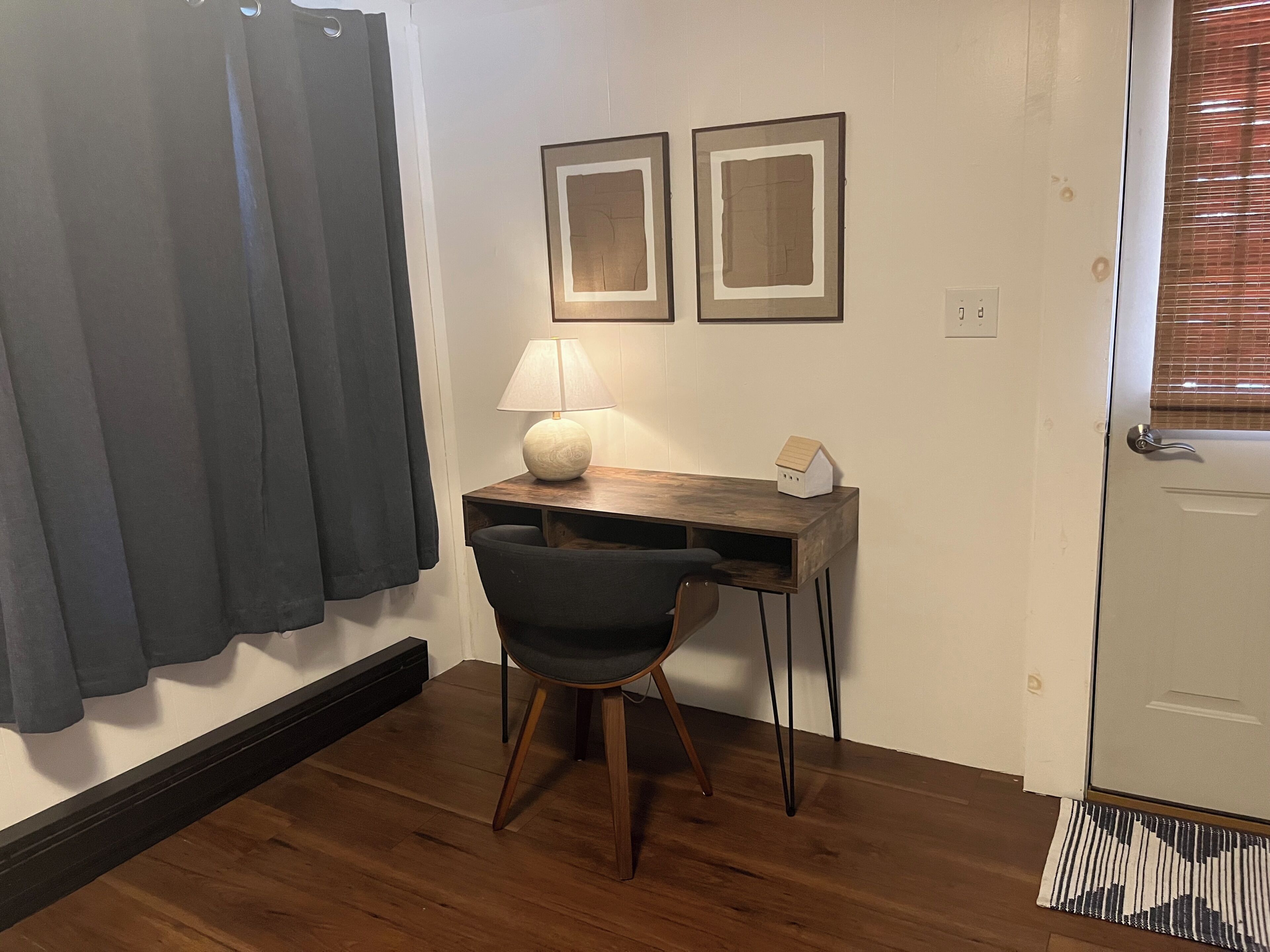Une pièce comprenant un bureau, une chaise, une lampe et deux tableaux encadrés accrochés au mur.