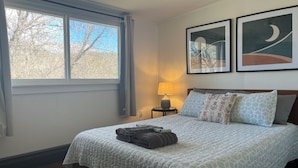 A bedroom with a bed, a nightstand, a lamp, and two framed artworks on the wall.