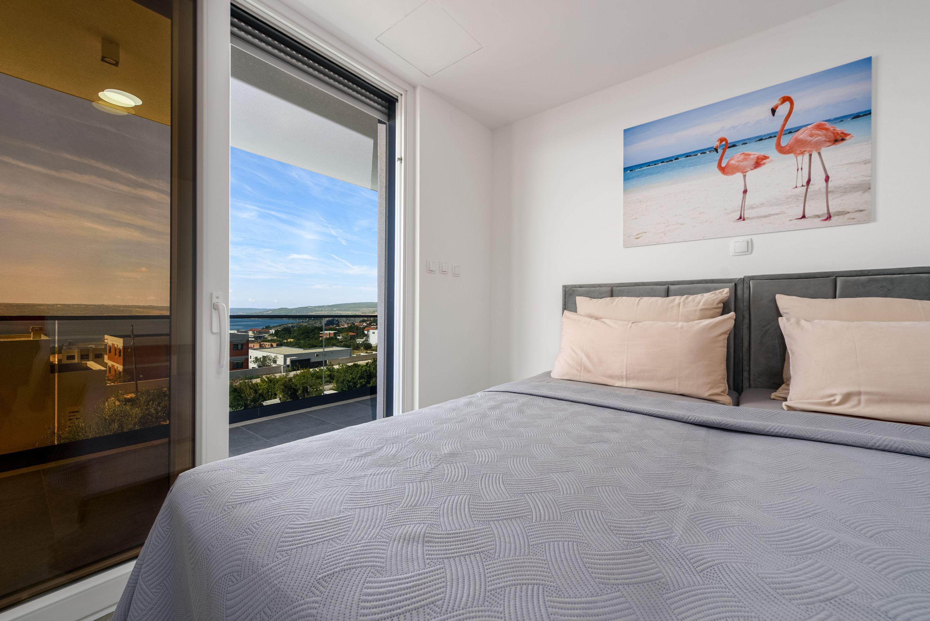 A hotel room with a bed, a large window with a city view, and a painting of flamingos on the wall.