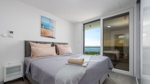 A bedroom with a bed, a nightstand, a painting, and a view through a sliding glass door. - Villa Solina Zadarvillas (Jasenice)