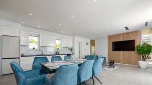 A modern kitchen with white cabinets, a dining area with blue chairs, a large TV, and a potted plant. - Villa Solina Zadarvillas (Jasenice)
