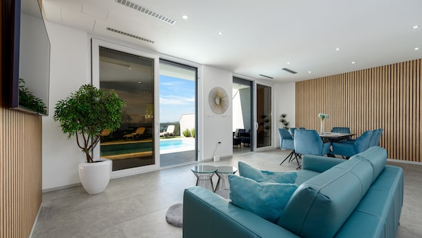 A modern living room with a teal sofa, a large potted plant, and a dining area with blue chairs. - Villa Solina Zadarvillas (Jasenice)