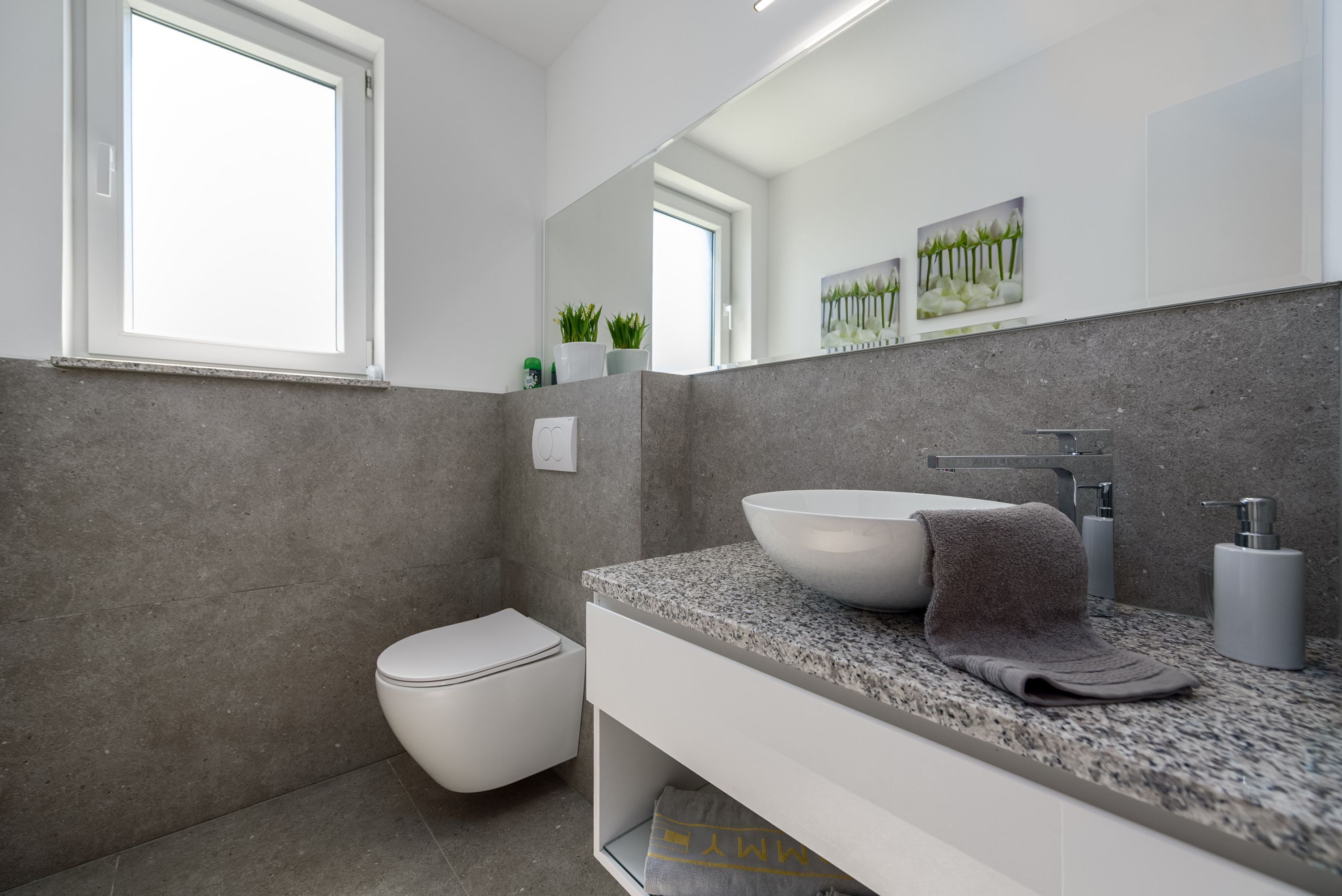 A modern bathroom with a white toilet, a granite countertop, a vessel sink, and a towel.