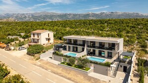 A modern two-story house with a swimming pool, a road in the foreground, and mountains in the background. - Villa Adriatique & Solina Zadarvillas (Jasenice)