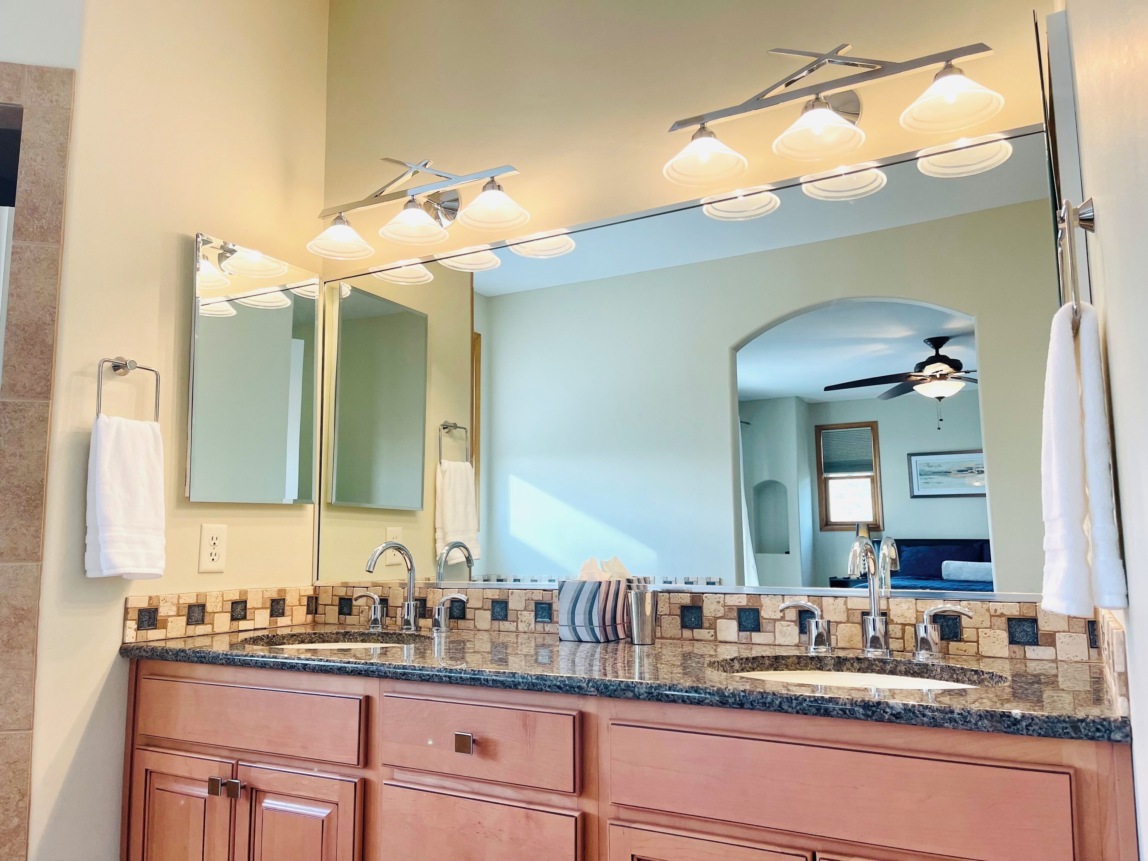 A bathroom with a double sink, a large mirror, and a ceiling fan.