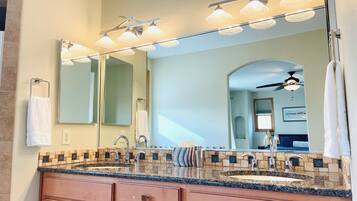 A bathroom with a double sink, a large mirror, and a ceiling fan.
