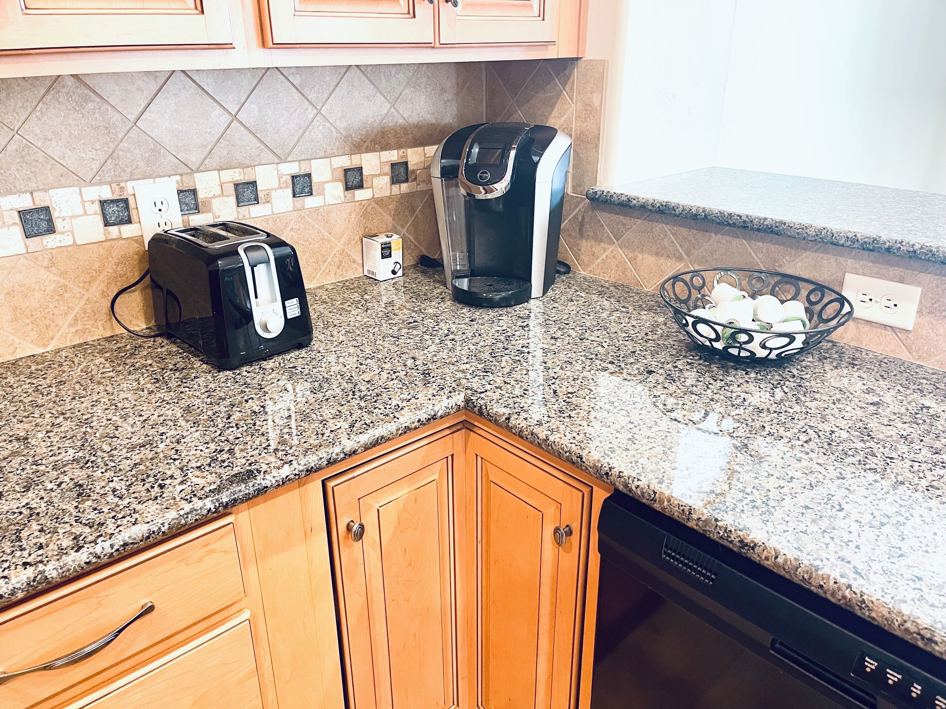 A kitchen with granite countertops, a toaster, a coffee maker, and a bowl of fruit.