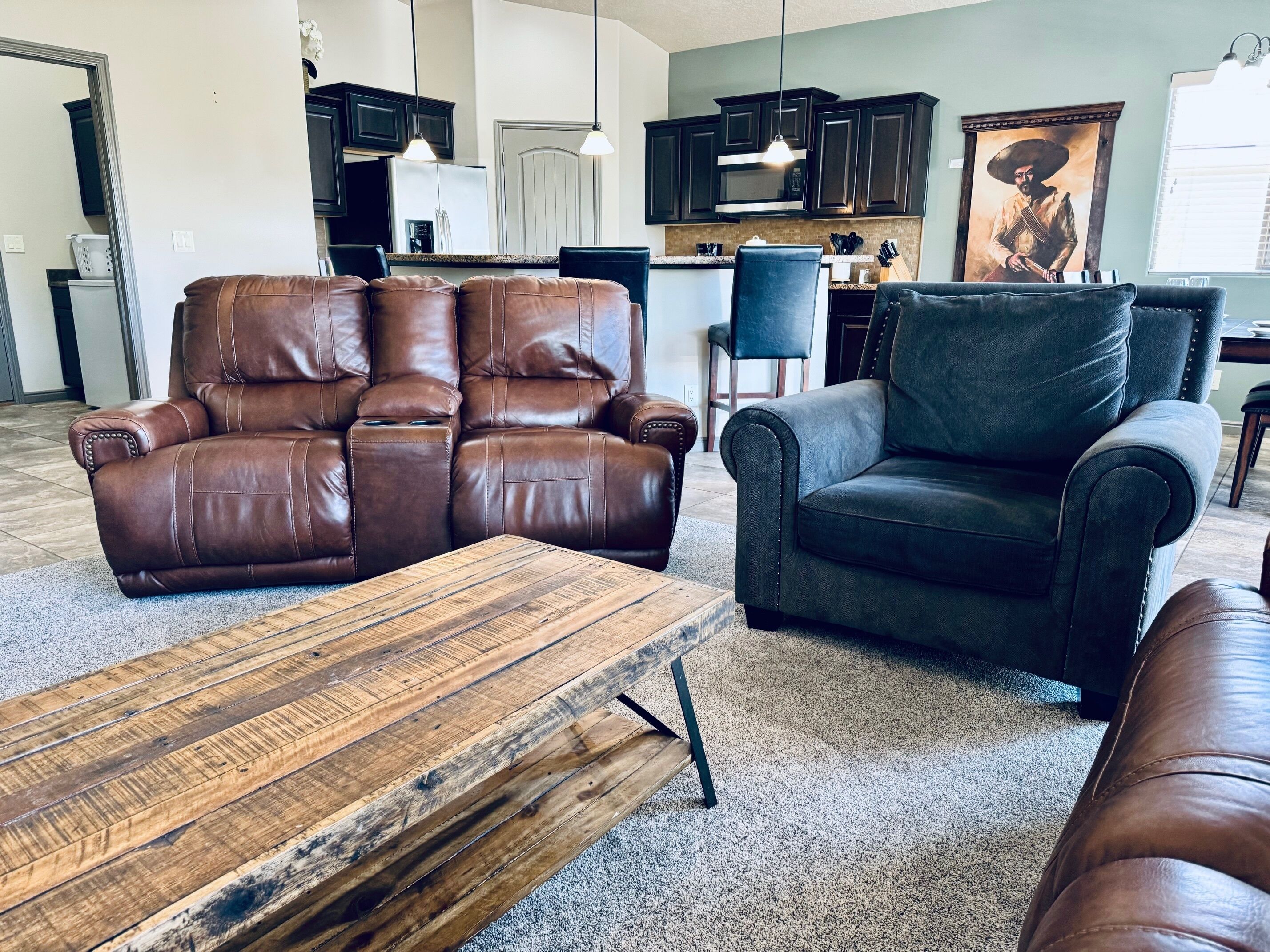 A living room with a brown leather sofa, a dark grey armchair, and a wooden coffee table.