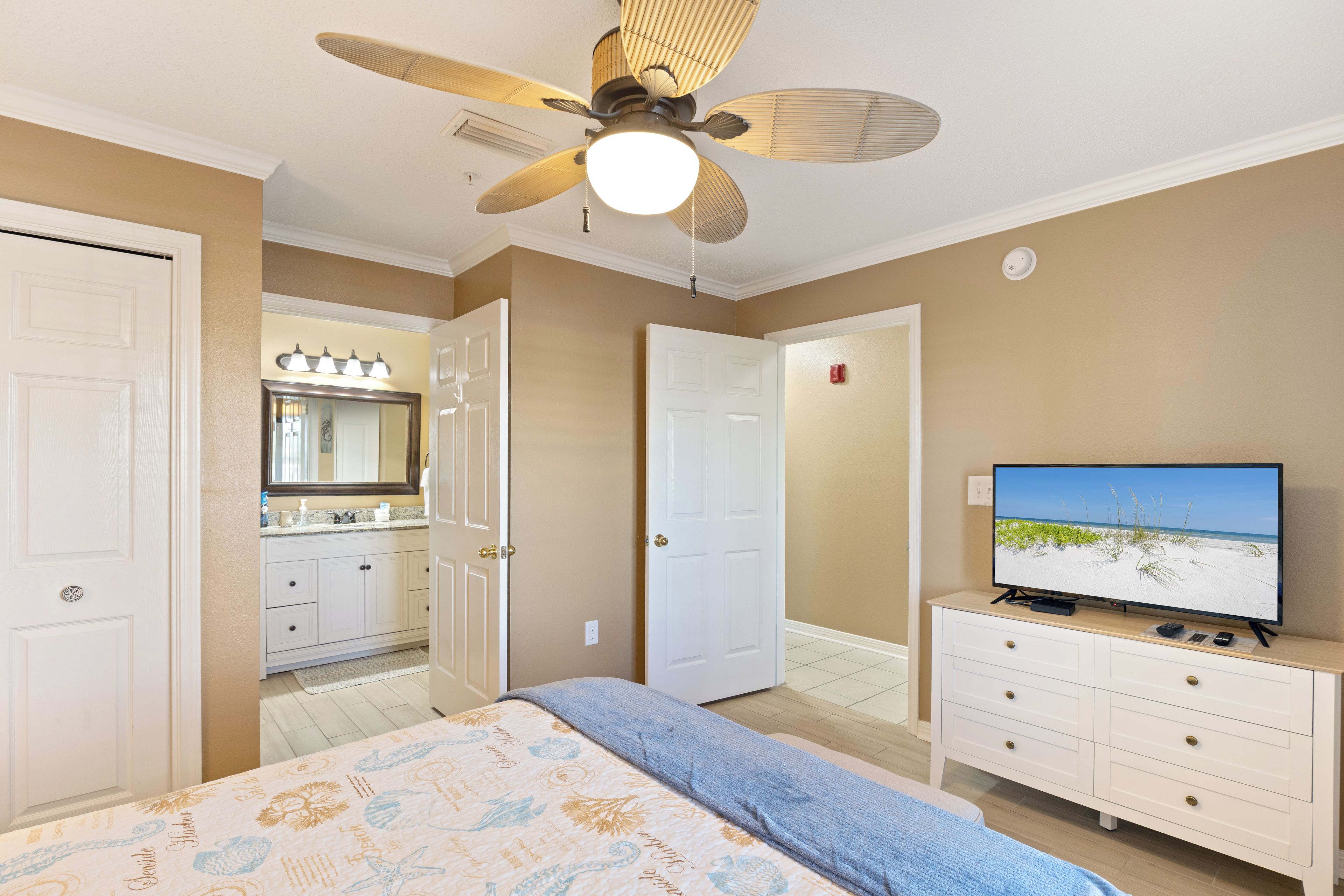 A bedroom with a bed, a television, a ceiling fan, and a bathroom with a mirror and sink.
