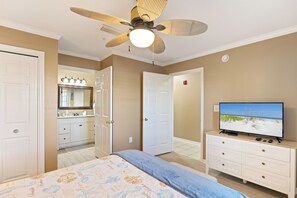 A bedroom with a bed, a television, a ceiling fan, and a bathroom with a mirror and sink. - Condo Near Beach with Pool PKRM (Pensacola)