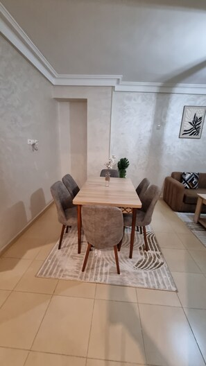 A dining area with a rectangular table, four chairs, a rug, a potted plant, and a sofa with a cushion. - The pearl of Marrakech (Marrakesh)