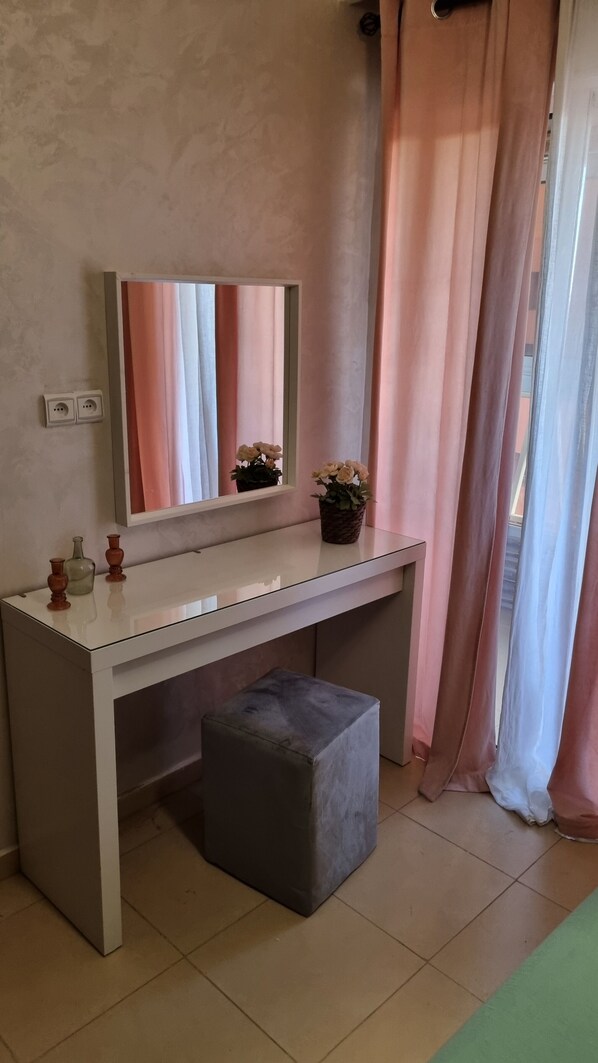 A room with a white desk, a mirror, a grey ottoman, a vase with flowers, and pink curtains. - The pearl of Marrakech (Marrakesh)