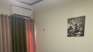 A room with a bed, an air conditioning unit, a wall-mounted thermostat, and a painting of rocks. - Cozy 1-bedroom apartment in perfect Kingston with AC (Kingston)