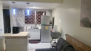 A compact kitchen with a refrigerator, a microwave, a sink, and a window with a brick pattern. - Cozy 1-bedroom apartment in perfect Kingston with AC (Kingston)
