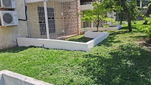 A courtyard with a white metal fence, a small tree, and a building with air conditioning units. - Cozy 1-bedroom apartment in perfect Kingston with AC (Kingston)