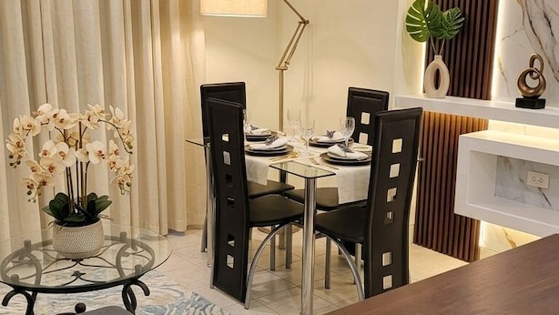A modern dining area with a table set for four, a sofa, and a small side table with a vase of flowers. - Cozy 1-bedroom apartment in perfect Kingston with AC (Kingston)