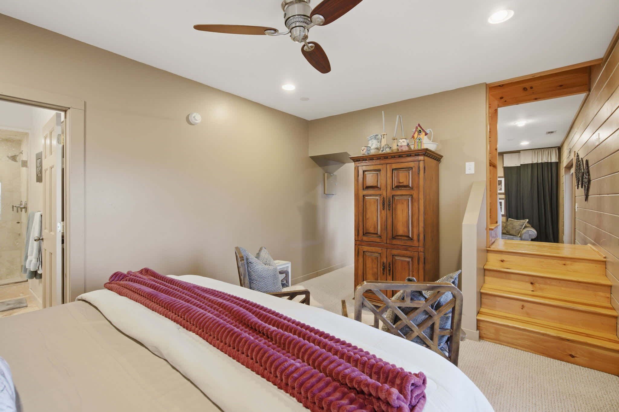 A bedroom with a bed, a wooden wardrobe, a chair, a desk, and a staircase.