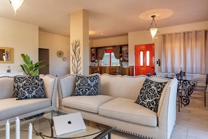 A living room with a sofa, a glass coffee table, and a laptop. There is a dining area with a table and chairs. - Sea view villa Noemi (Kato Gouves)
