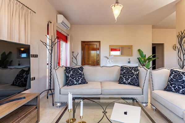 A living room with a sofa, a coffee table, a TV, and a laptop. - Sea view villa Noemi (Kato Gouves)