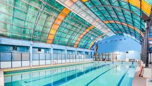An indoor swimming pool with a glass ceiling, blue walls, and a tiled floor. - Super Deluxe Room Palette Country Club (Surat)