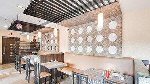 A restaurant with high ceilings, a staircase, and a wall with circular cutouts. Tables and chairs are arranged for dining. - Super Deluxe Room Palette Country Club (Surat)