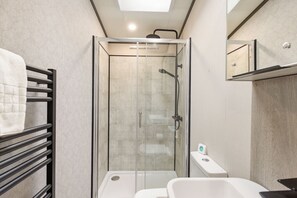 Een moderne badkamer met een douche met glazen wand, een witte wastafel en een handdoekrek.