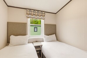 Een kamer met twee bedden, een kleintje tafeltje en een raam met uitzicht op een groen gebouw.