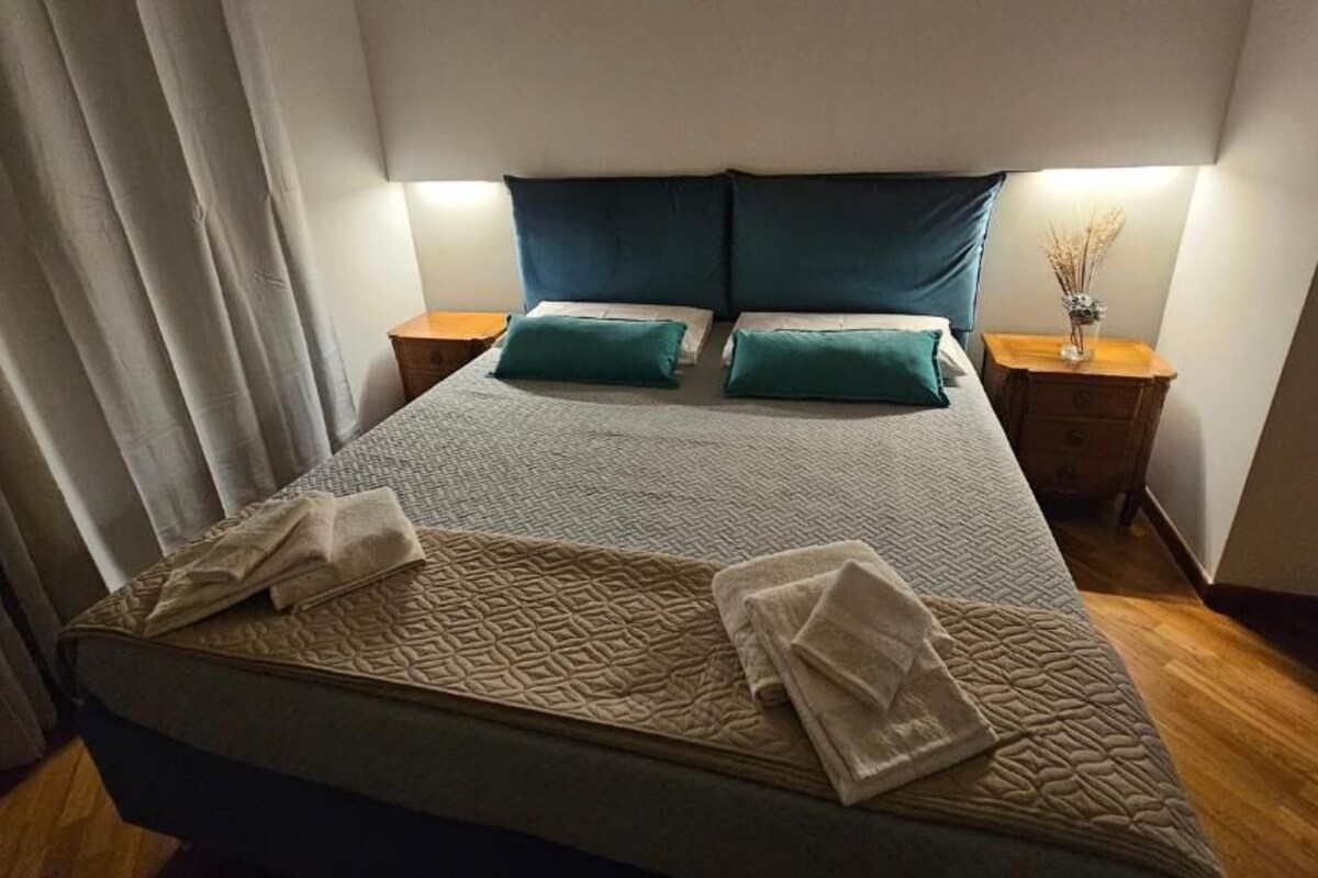A neatly made bed with a patterned bedspread, two pillows, and a bedside table with a lamp.