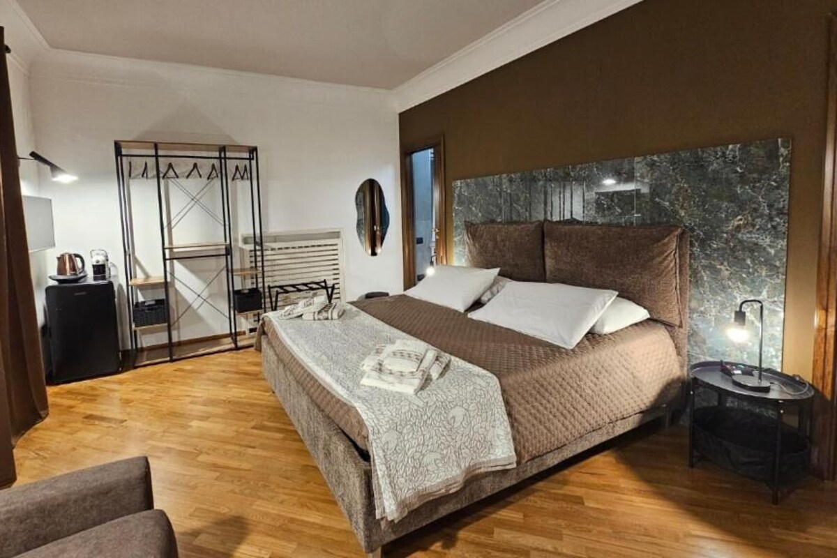 Une chambre avec un grand lit, une table de chevet, une armoire et une vue sur l’extérieur.