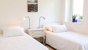 Quarto com duas camas de solteiro, mesa de cabeceira com duas luminárias, janela com vista e um quadro na parede.