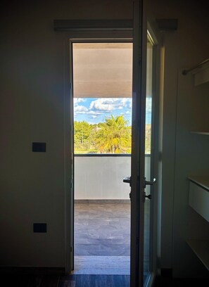 Een open deur die leidt naar een balkon met uitzicht op bomen en een heldere lucht.