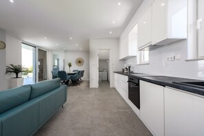 Eine moderne Küche mit weißen Schränken, einer schwarzen Arbeitsplatte und einem Essbereich mit einem türkisblauen Sofa und Stühlen.