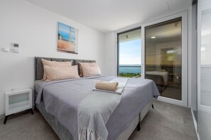 A bedroom with a bed, a nightstand, a painting, and a view through a sliding door. - Villa Adriatique Solina Zadarvillas (Jasenice)