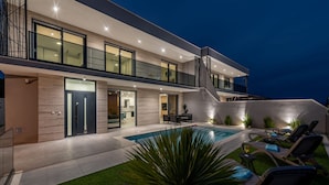 Una moderna casa a due piani con piscina, area salotto esterna e un balcone ben illuminato.