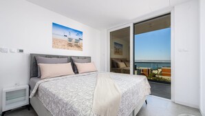 Una camera da letto con un letto, un comodino, un'ampia finestra vista mare e una porta che dà su un balcone.