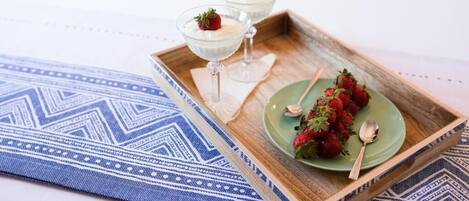 A tray with two glasses of a creamy dessert topped with strawberries, a plate with more strawberries, and a spoon on a blue patterned cloth.