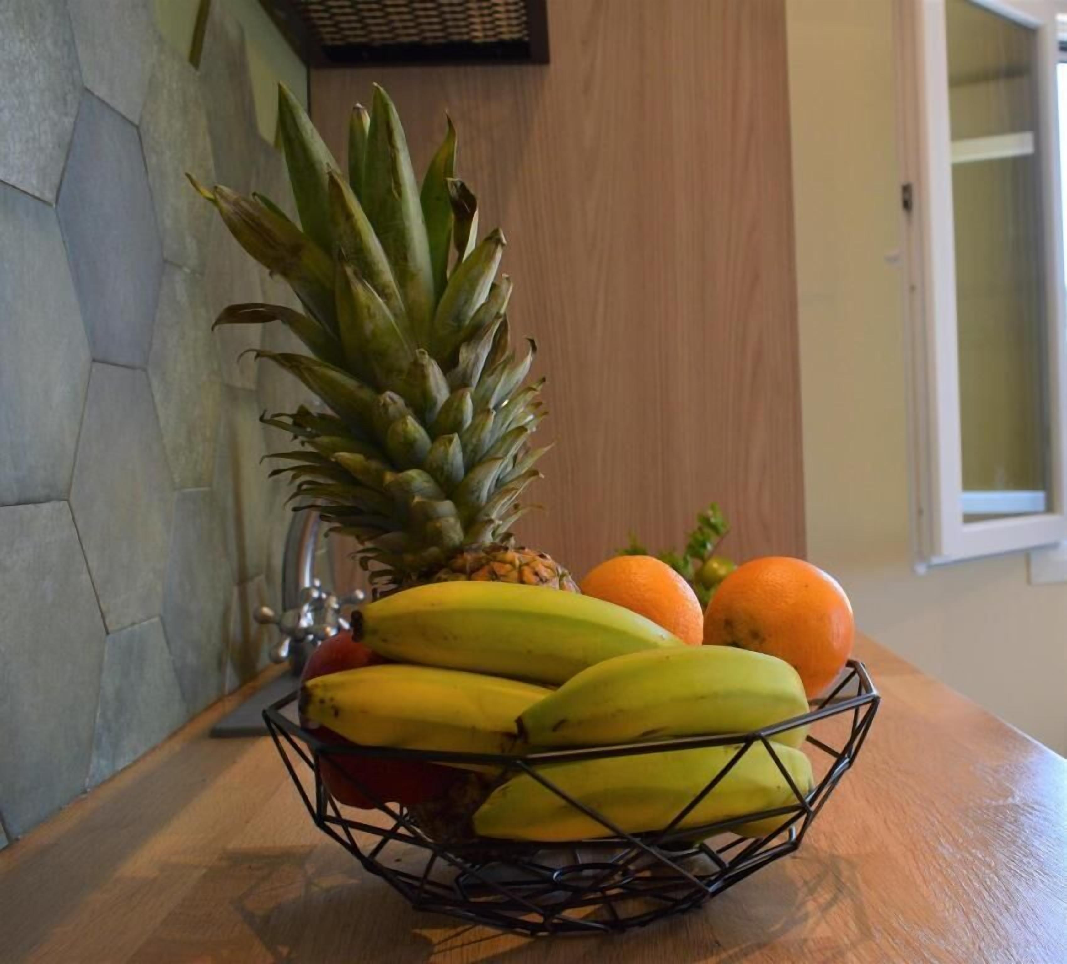 Un panier de fruits contenant des bananes, des oranges et un ananas, posé sur une table en bois.