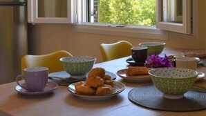 Un comedor con una mesa dispuesta para el desayuno, que incluye croissants y una taza, cerca de una ventana con vistas abiertas a zonas verdes.