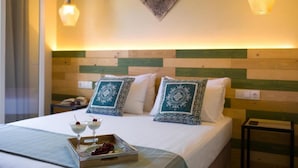 Habitación de hotel con cama, mesitas de noche, almohadones decorativos y una bandeja con un postre.