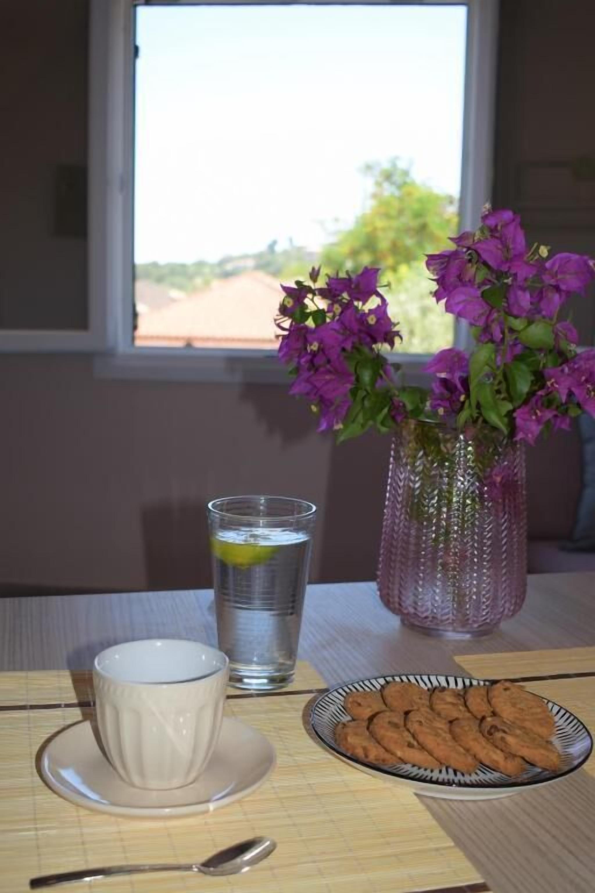 Une table avec une tasse, un verre, une assiette de biscuits et un vase de fleurs.