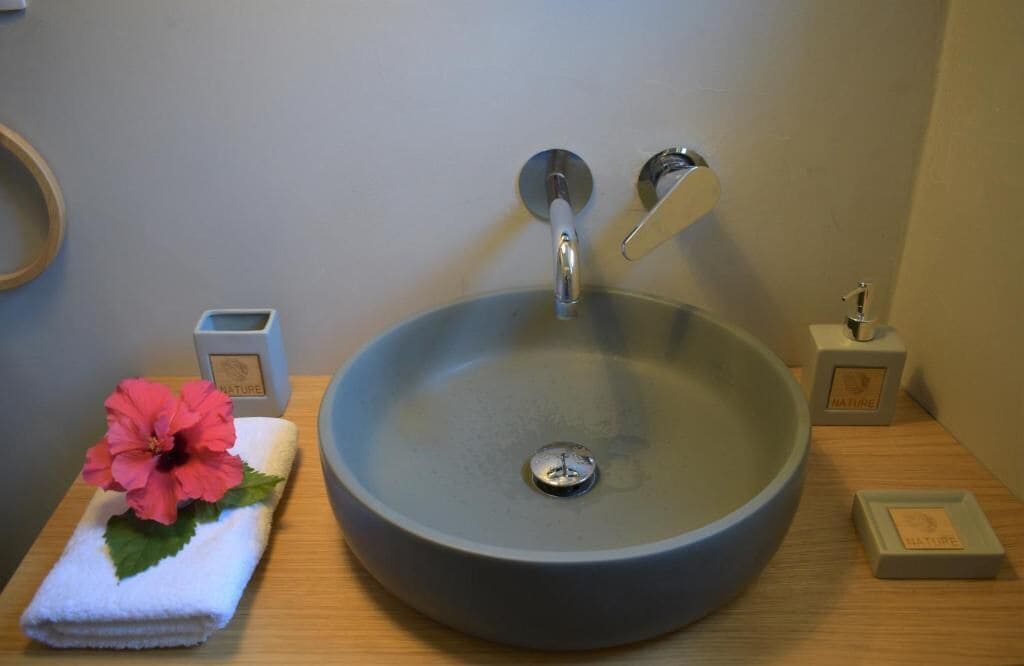 Een badkamermeubel met een wasbak, een enkele kraan, een bloem en twee zeepdispensers.